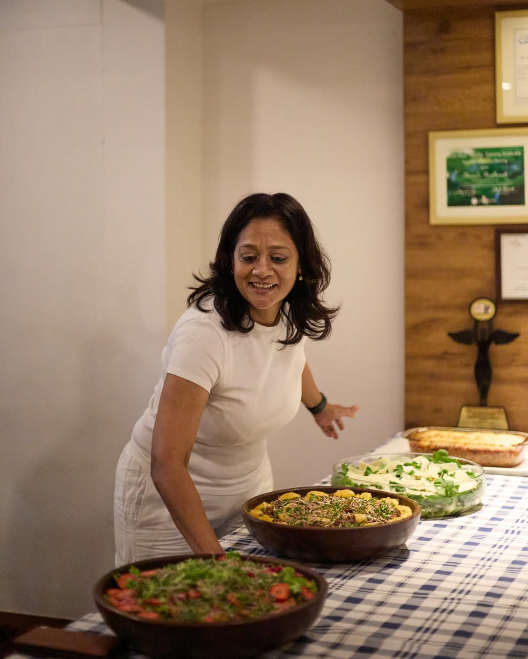 Sharmila smiling while arranging bowls of fresh salads and dishes on a checkered tablecloth.